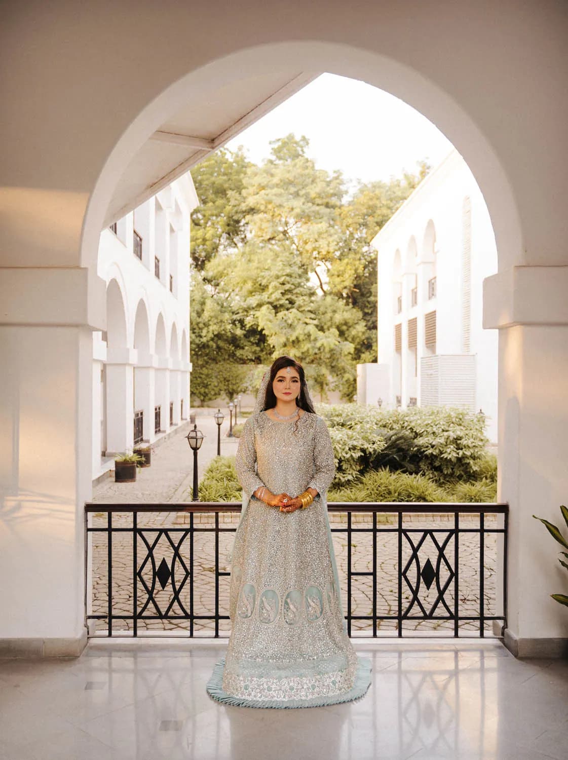 Bride under a white arch with a garden behind