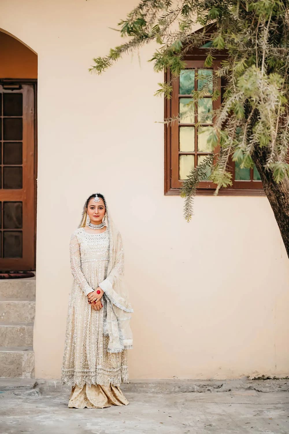 Bride standing by a cream wall and green window