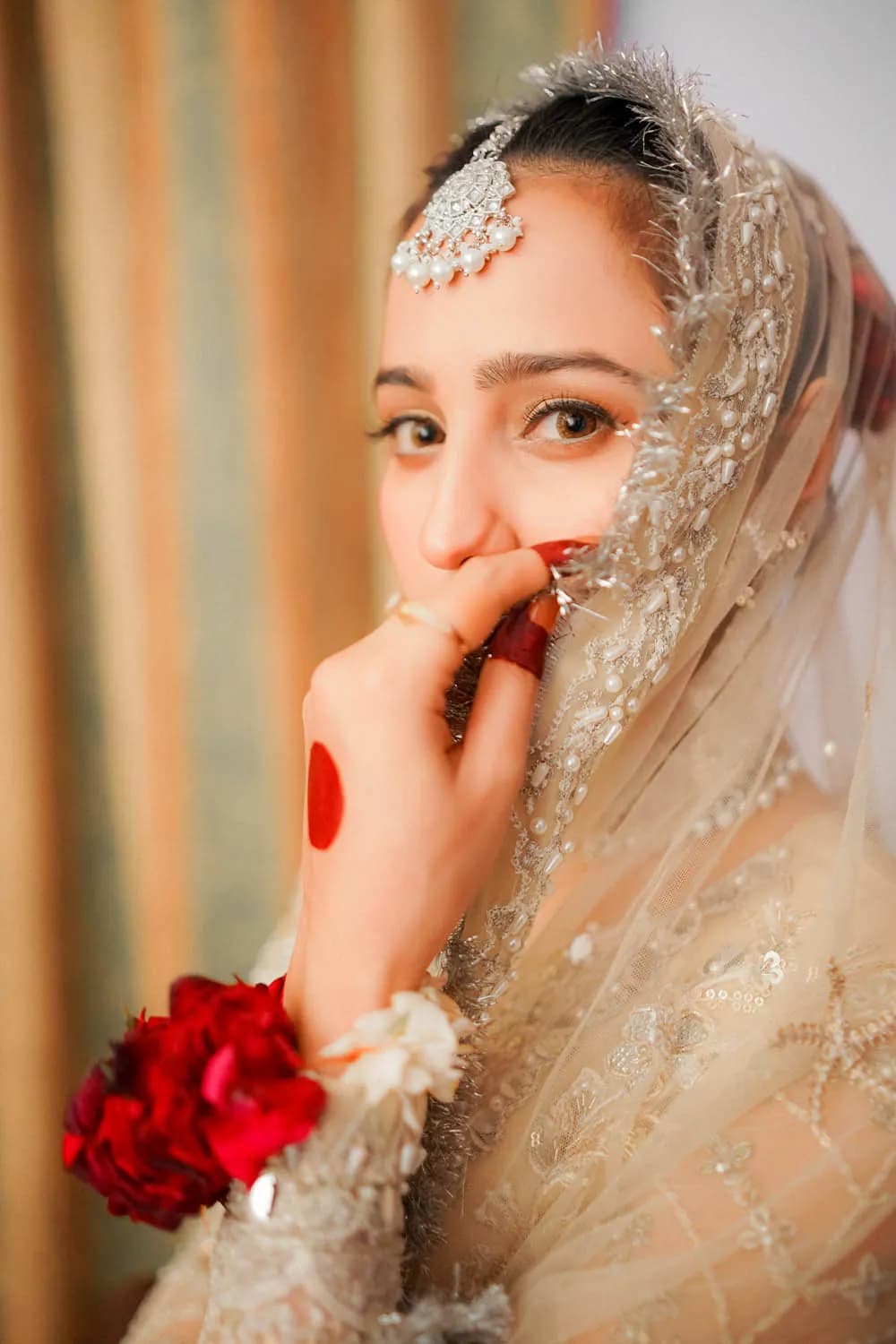 Bride smiling behind her veil with red roses