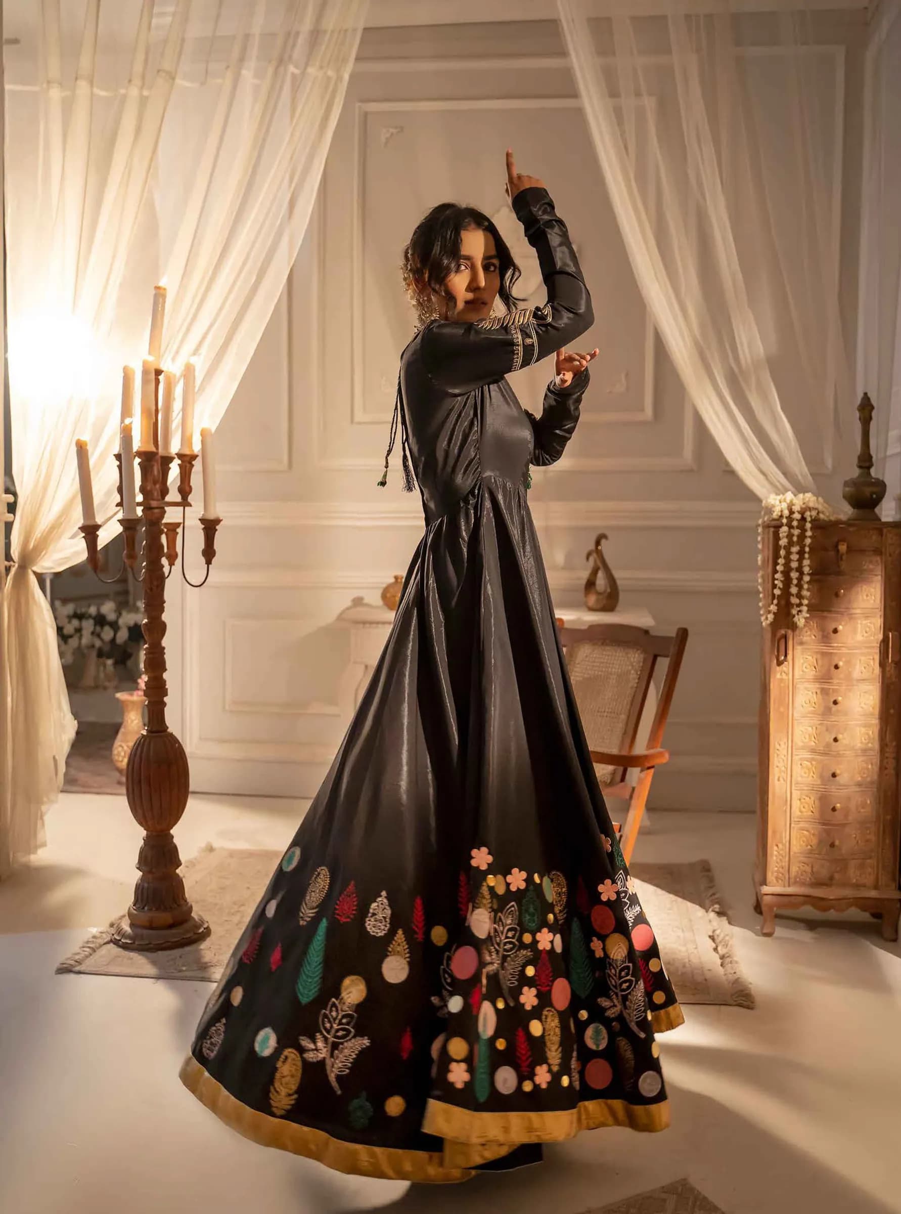 Model in an embroidered black gown beside candlelit drapes