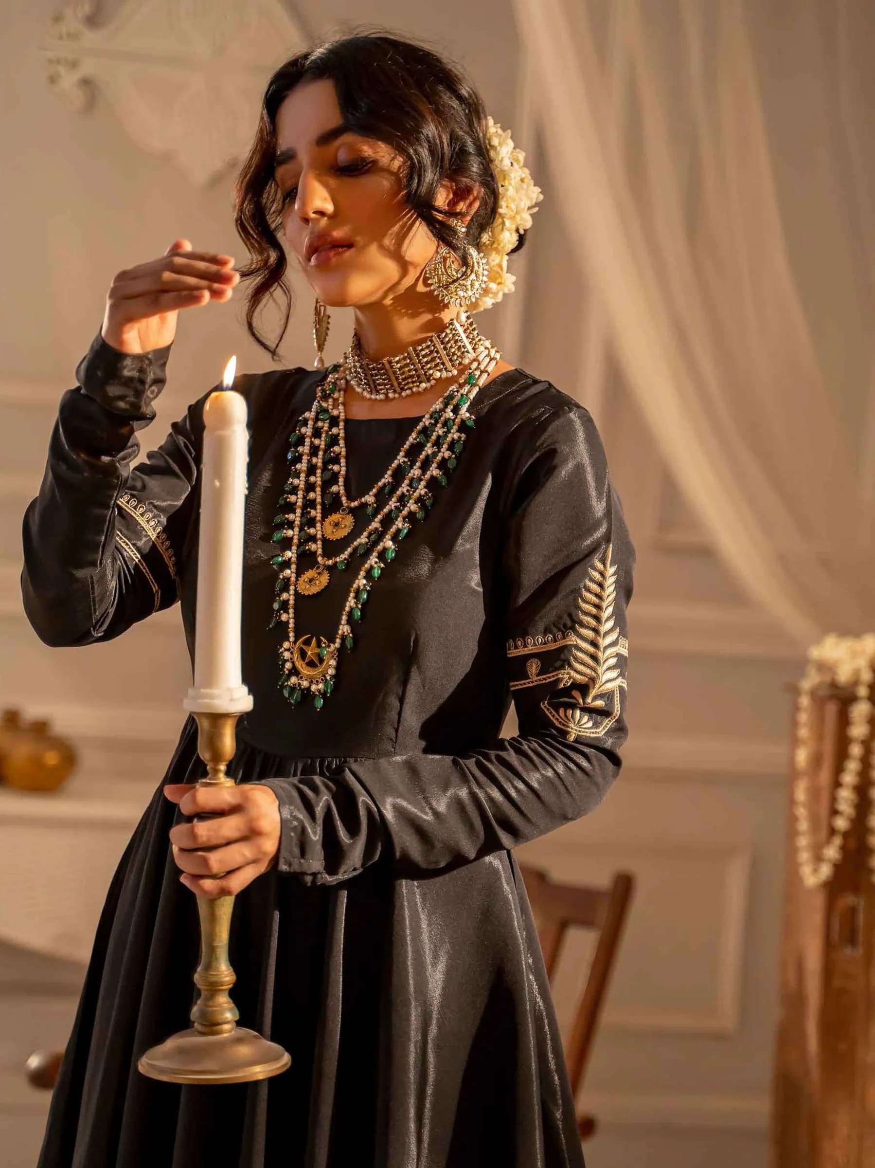 Model in black holding a candle against white curtains