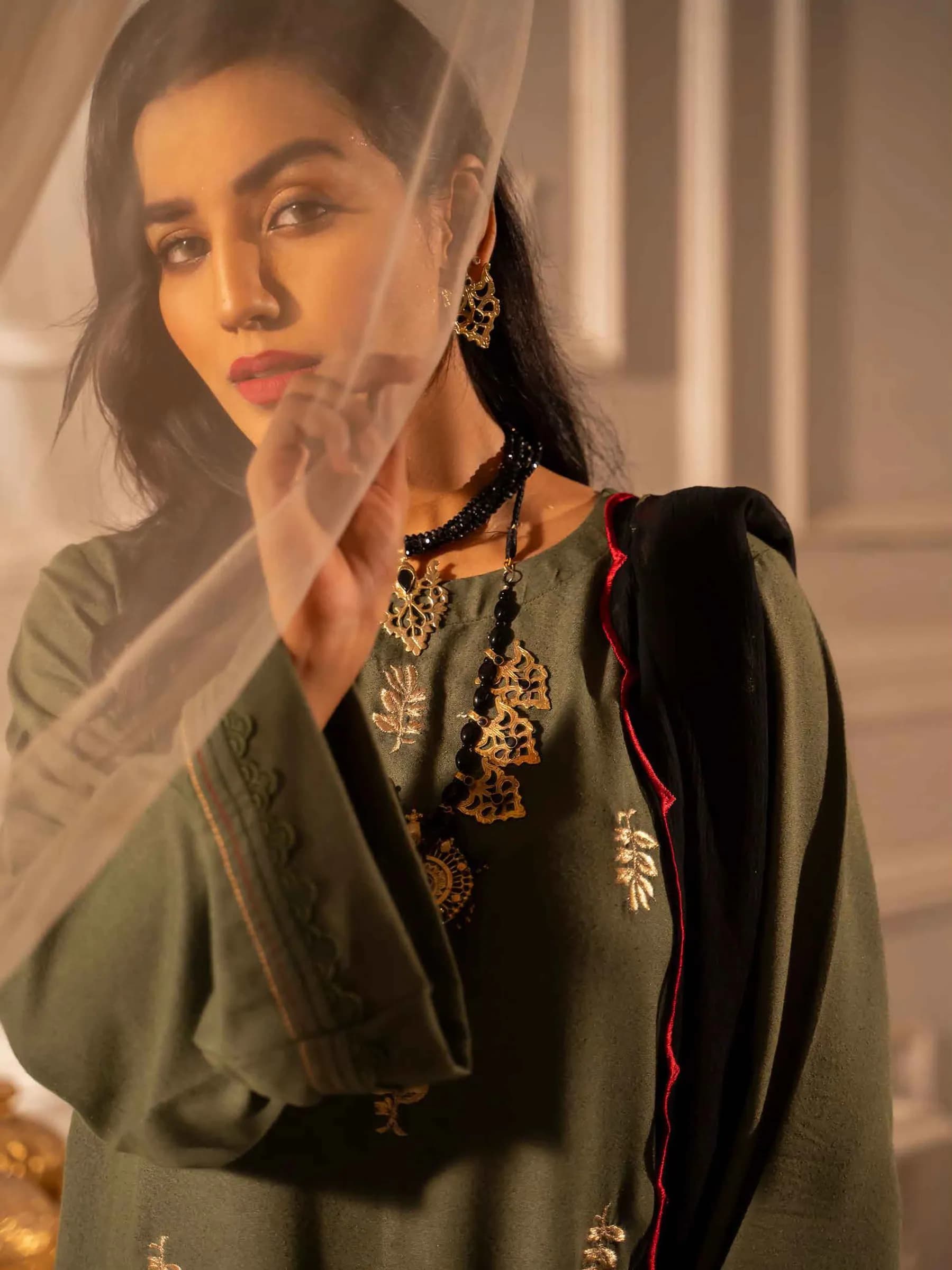 Model in a dark embroidered outfit by soft window light