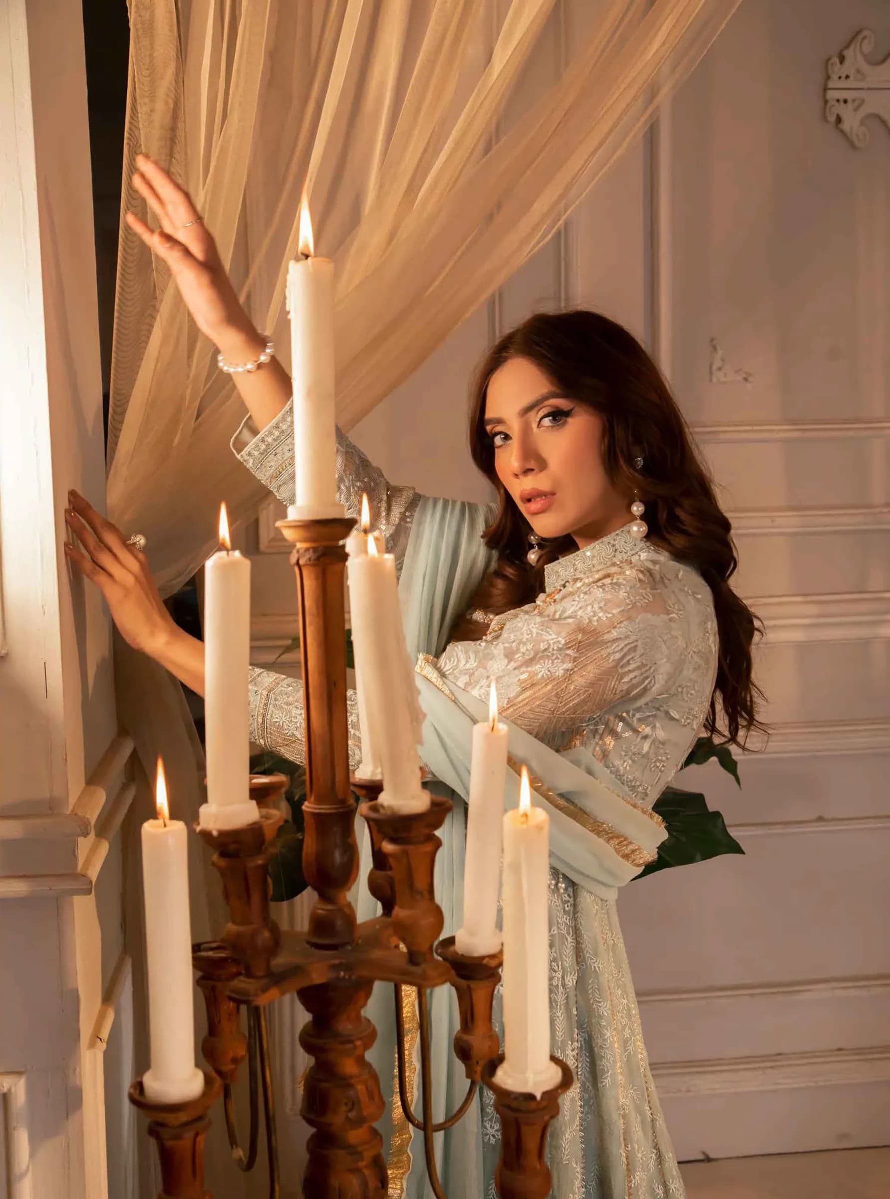 Model posing beside tall candles in a cream room