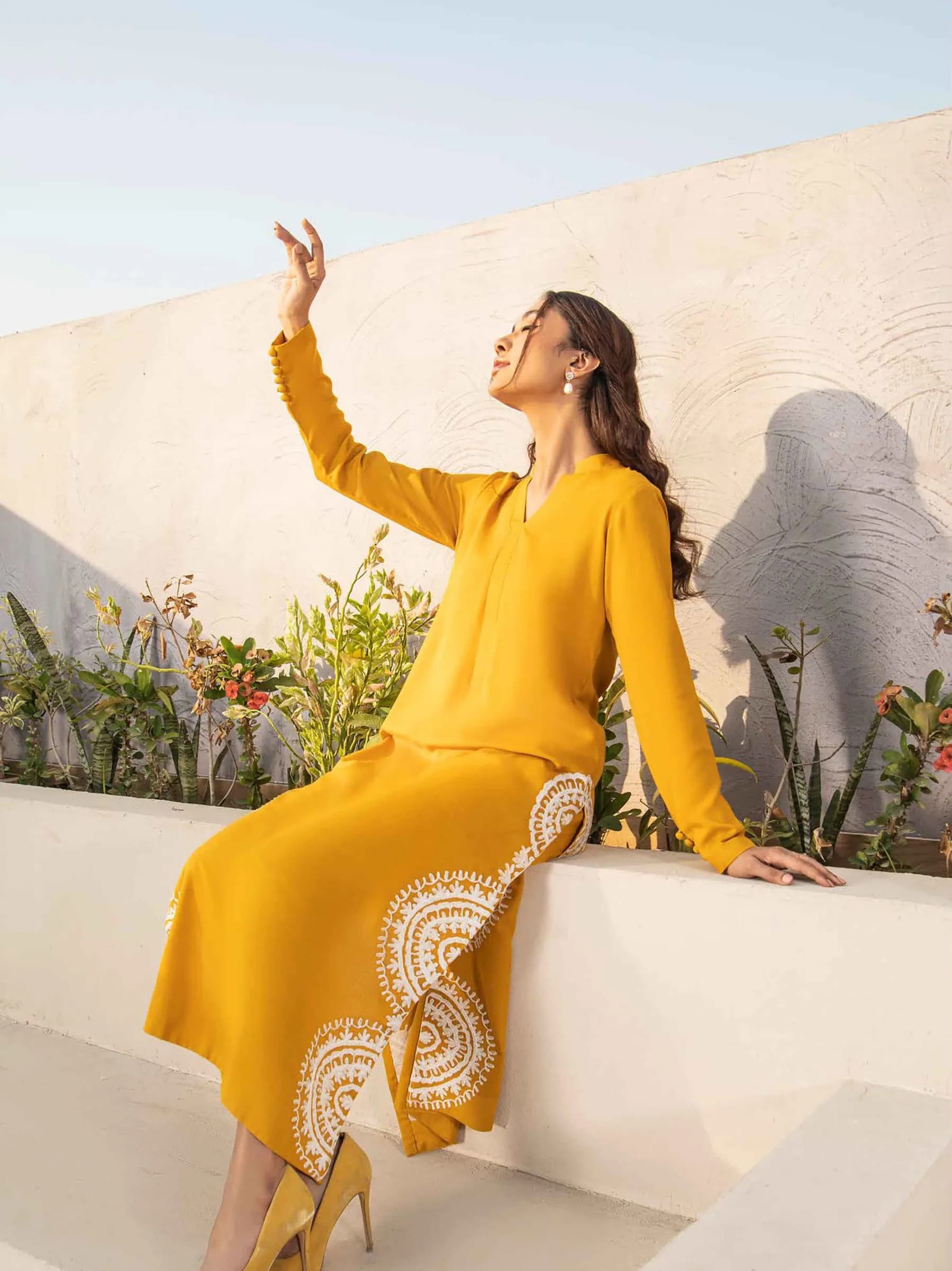 Model in mustard yellow seated on a white wall