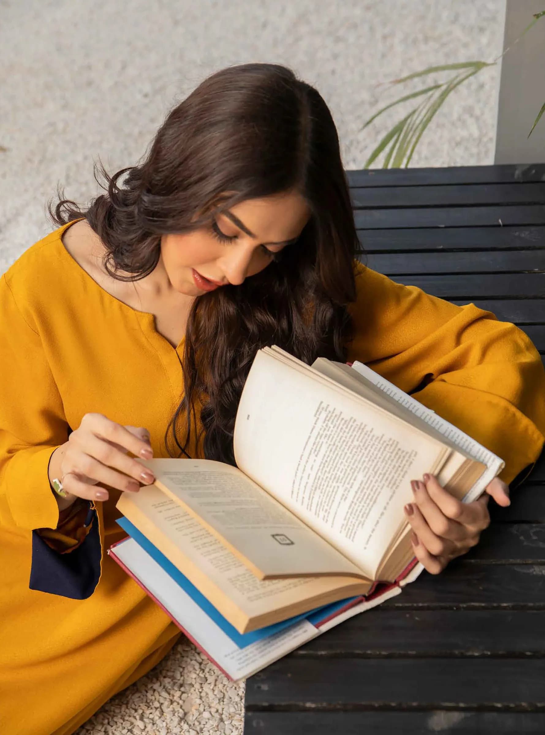 Model in mustard yellow reading a book
