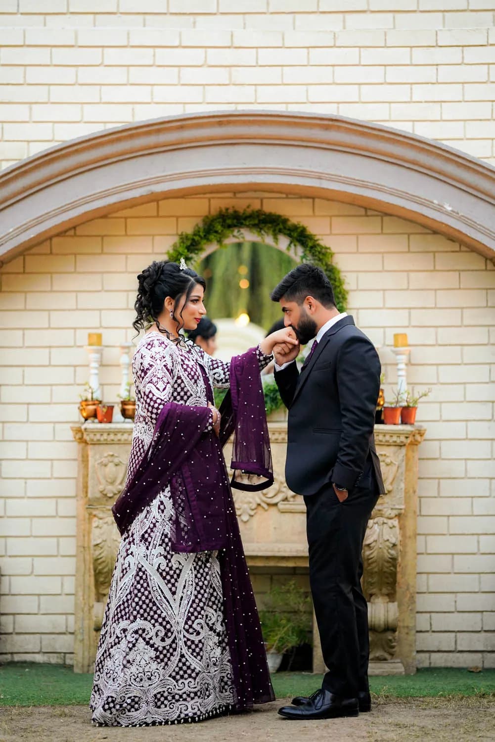 Groom kissing the bride's hand by a yellow brick arch