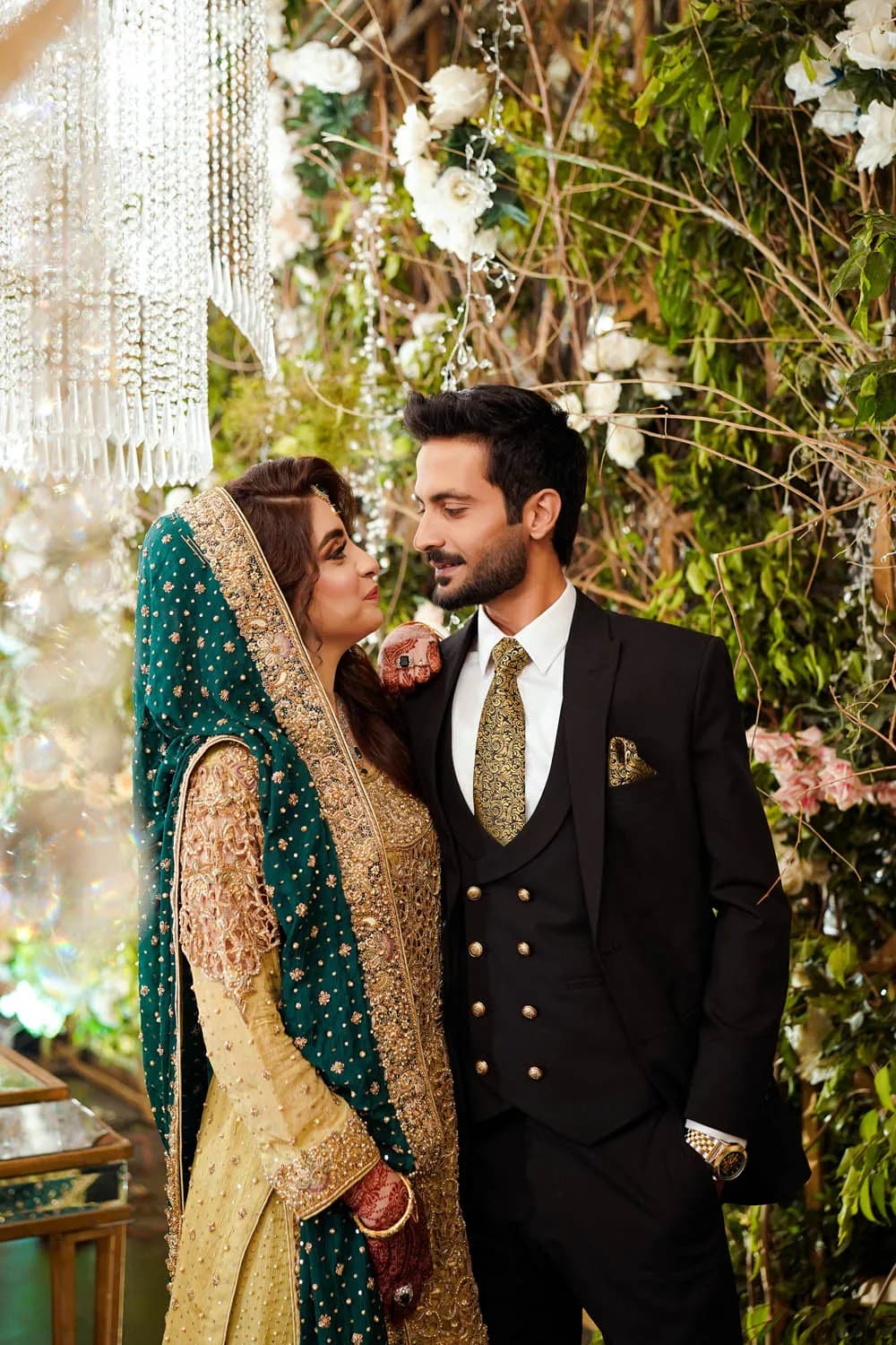 Groom in a black sherwani beside the bride under flowers