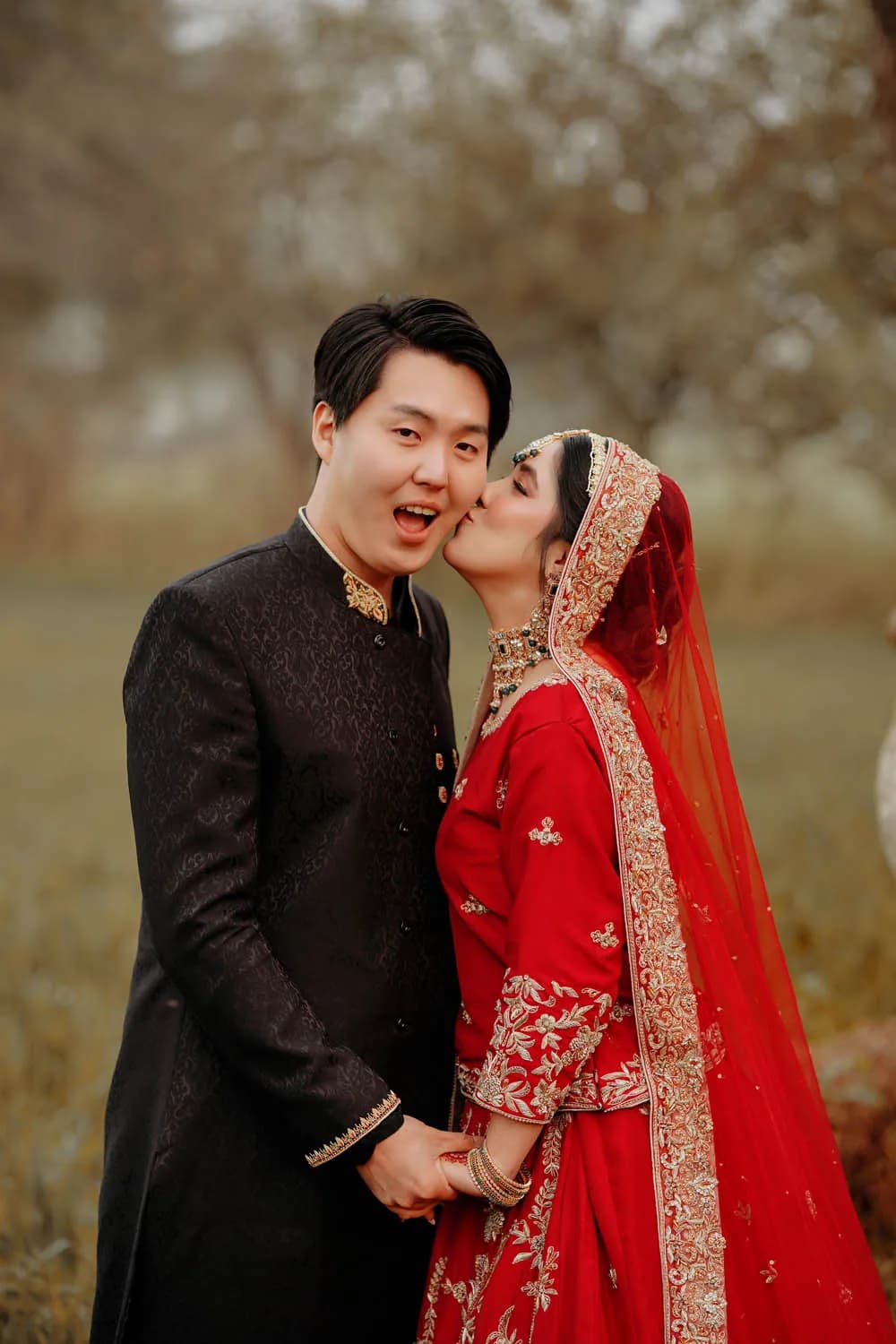 Couple in red bridal wear among autumn trees